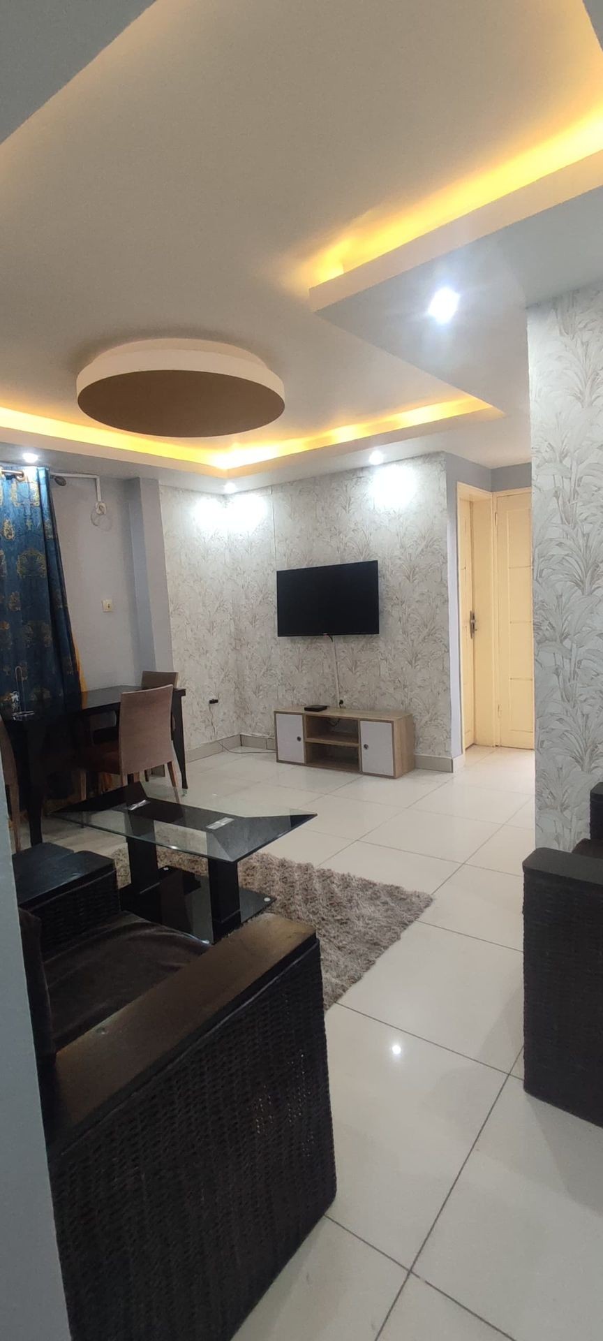 Modern living room with a round ceiling design, TV, and furniture on tiled floor.